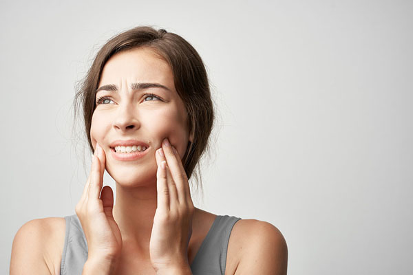 woman holding both sides of her mouth in pain from her teeth